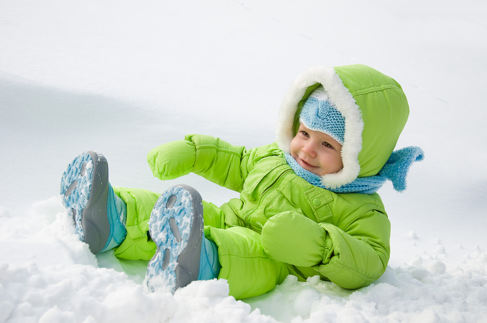 Kind liegt im Schnee mit Schneeanzug