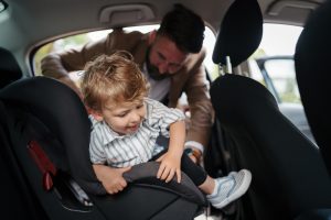 Mann beugt sich ins Auto zu Kind im Kindersitz